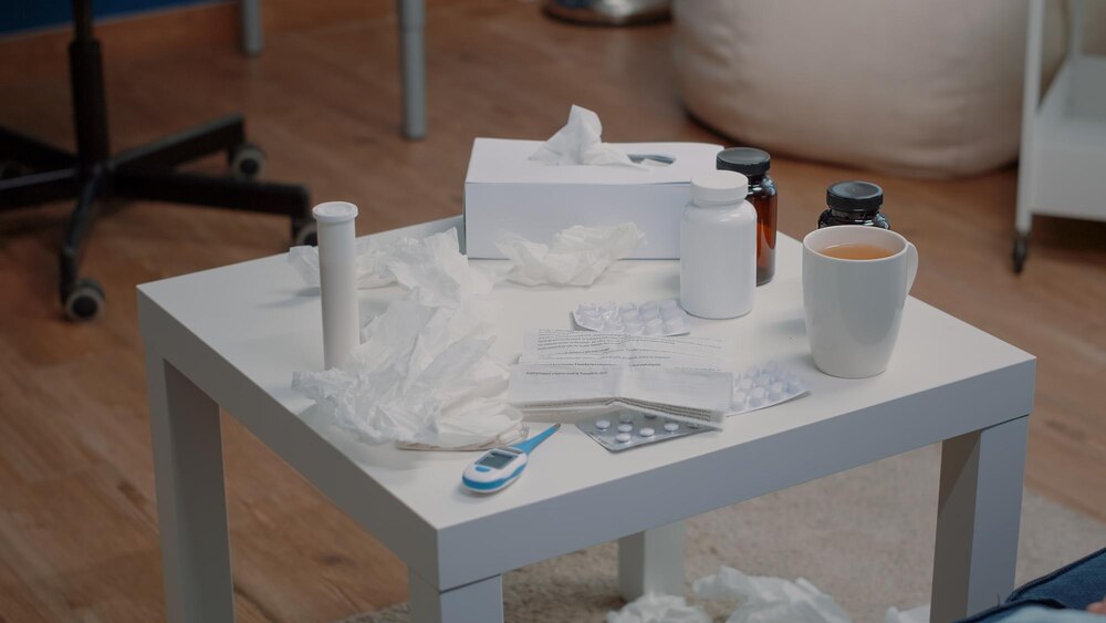 Close up of table with treatment and medical tools against disease. Empty space with medicaments, bottles of pills, capsule tablets, thermometer, tissues and tea. Medication against illness