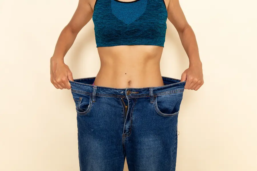 Front view of young female with fit body in blue shirt and jeans on light-white wall